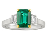 emerald and diamond trilogy ring with emerald-cut emerald framed by trapezoid diamonds on each shoulder. Two tone platinum and 18ct yellow gold. Made in The UK